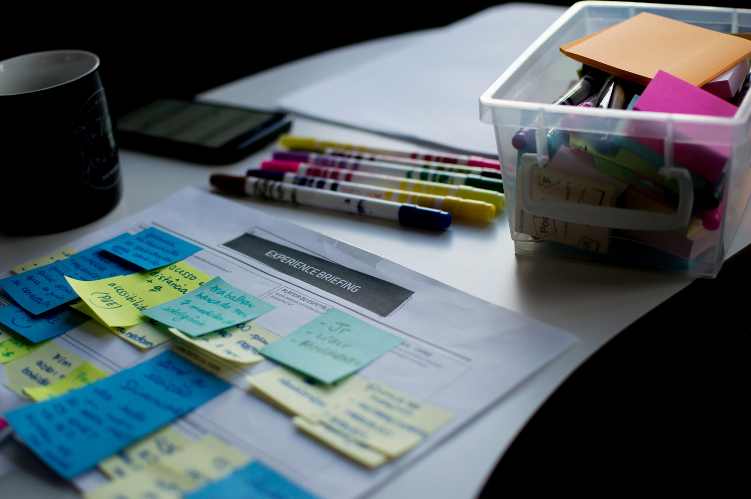 Image of a work desk with post-it notes, markers, and a bin of note-taking tools